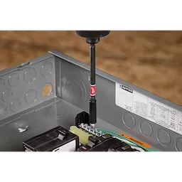 A SHOCKWAVE™ 6" Impact Magnetic Bit Holder is shown in use, attached to a drill and securing a screw into an electrical box. The magnetic bit holder is black with a red band and the SHOCKWAVE™ logo. Various tools and components are visible within the electrical box.