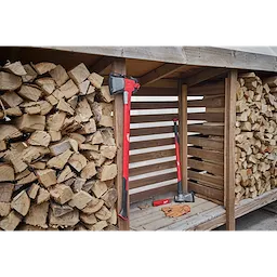 The product image features the Wood Splitting Family, which includes a red and black axe and a splitting maul arranged next to a large stack of split logs in a wooden storage shed. Gloves and another tool accessory rest on the wooden floor.