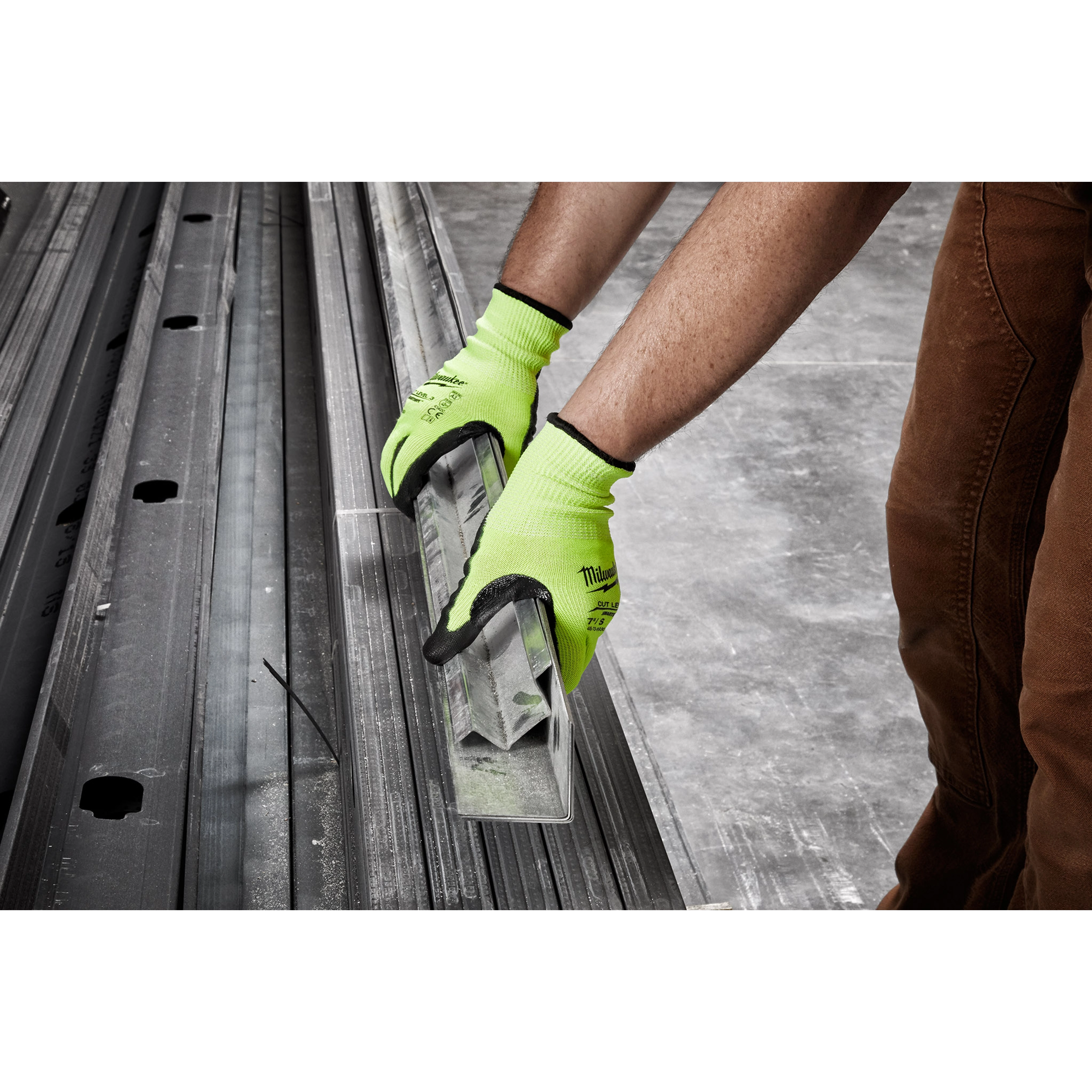 A person wearing Hi Vis Cut Gloves is holding metal bars over a concrete floor, showcasing the gloves' grip and protection.