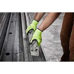 A person wearing Hi Vis Cut Gloves is holding metal bars over a concrete floor, showcasing the gloves' grip and protection.