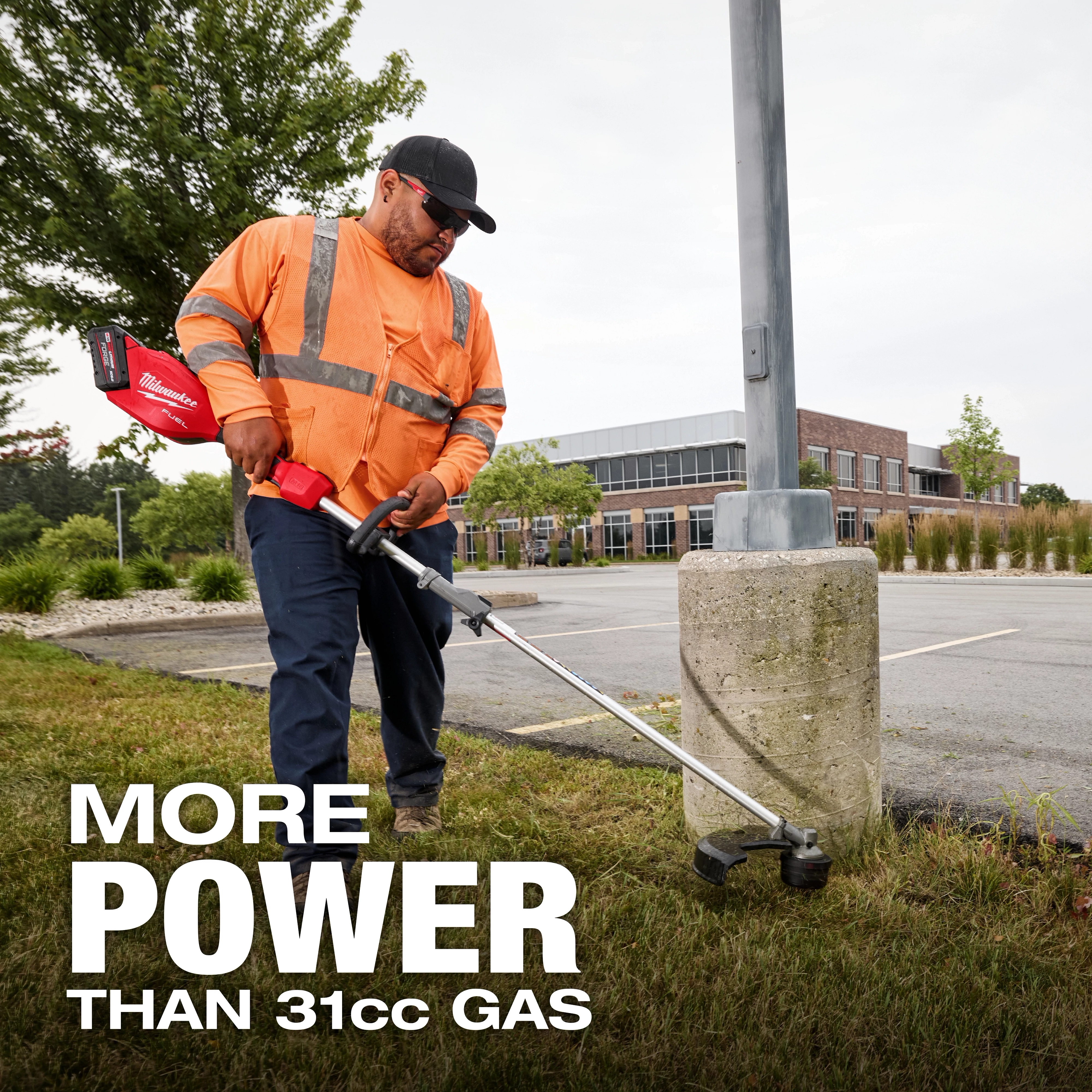 Worker trimming grass near a parking lot with the M18 FUEL String Trimmer w/ QUIK-LOK Kit.