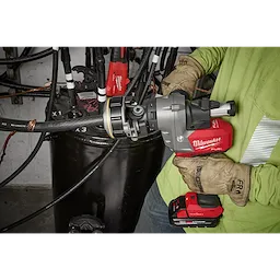 A person wearing gloves operates an M18 FUEL™ Covered Conductor Cable Stripper from Milwaukee Tool, stripping a cable in an industrial setting. The red and black power tool is seen in use, efficiently removing the cable's outer layer.