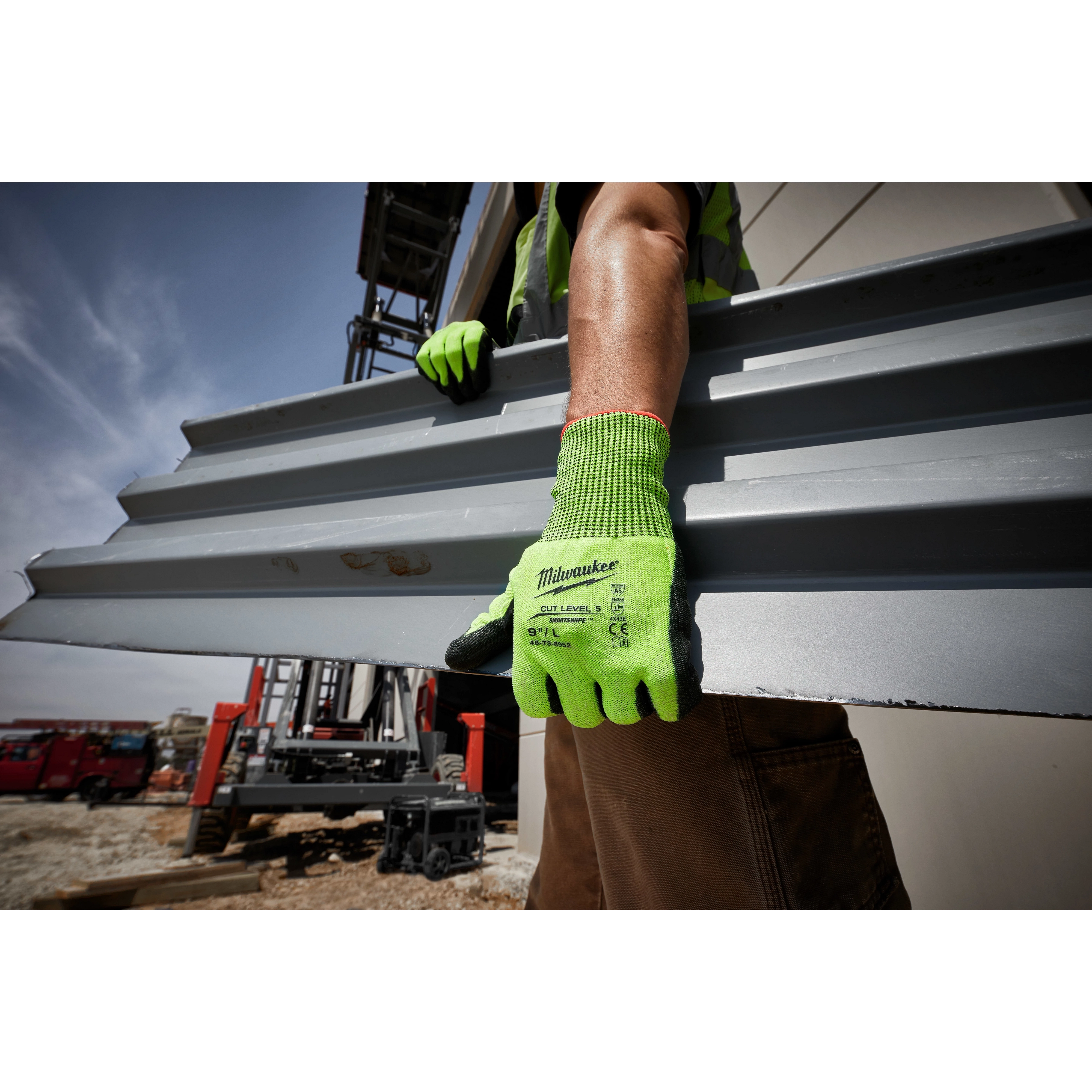 Worker wearing High Visibility Cut Level 5 Polyurethane Dipped Glove - L, holding a metal sheet at a construction site.