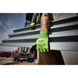 Worker wearing High Visibility Cut Level 5 Polyurethane Dipped Glove - L, holding a metal sheet at a construction site.