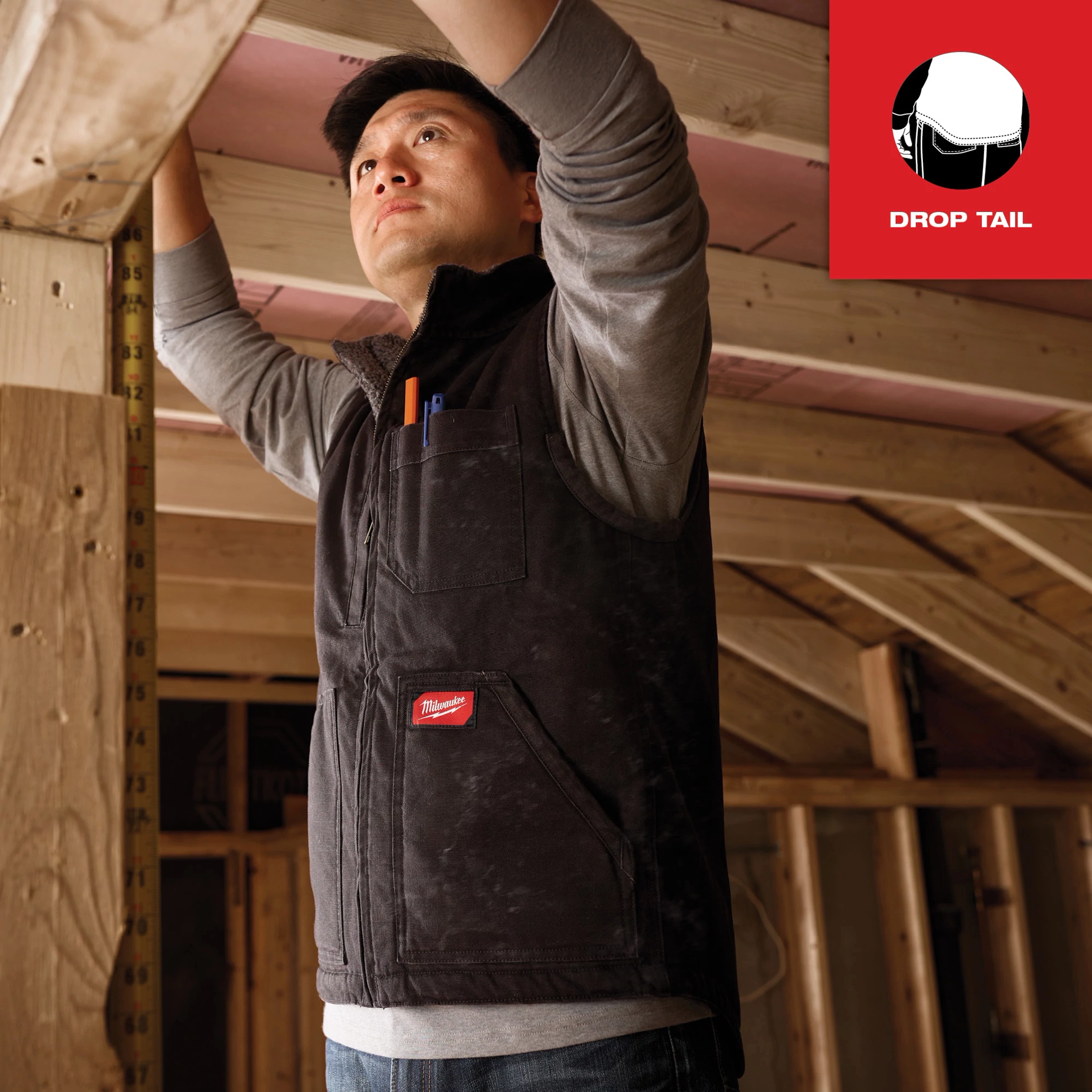 Person wearing a Heavy Duty Sherpa-Lined Vest in a construction setting, adjusting a wooden beam. Logo on the chest and pocket.