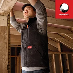 Person wearing a Heavy Duty Sherpa-Lined Vest in a construction setting, adjusting a wooden beam. Logo on the chest and pocket.