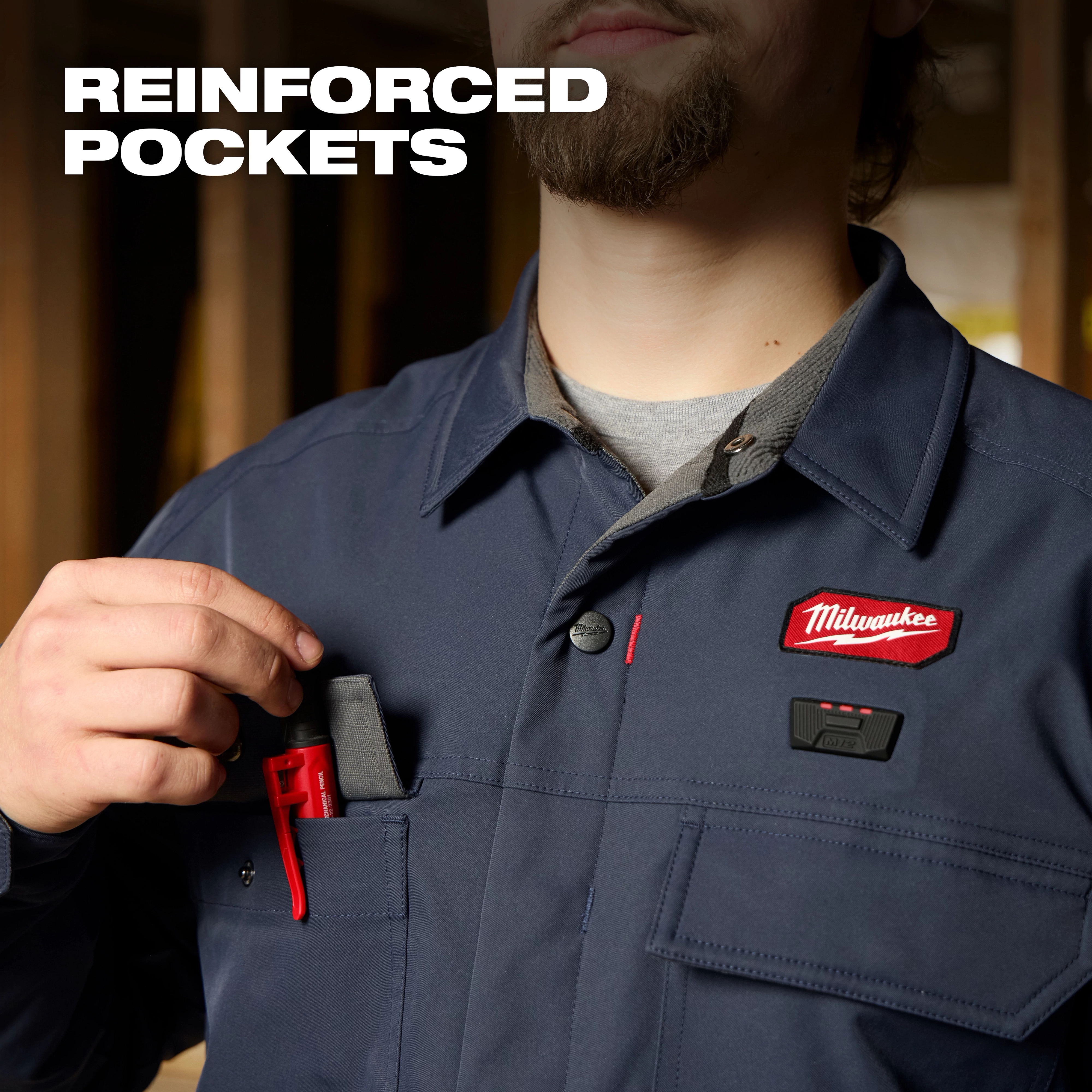 Person wearing an M12 Shirt Jacket - Navy L using a reinforced chest pocket to hold a small red tool.