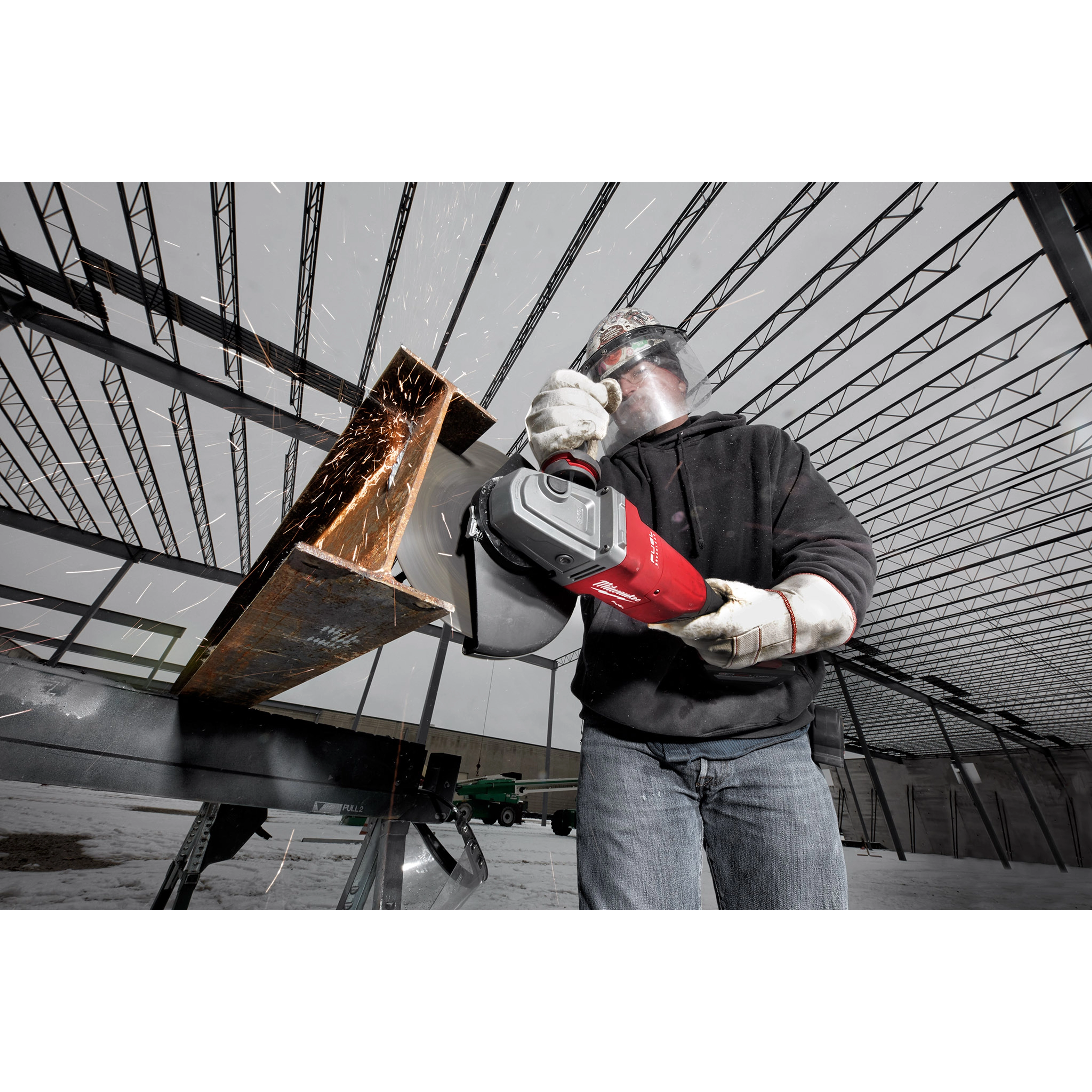 A worker uses the M18 FUEL 7” / 9” Large Angle Grinder (LAG) to cut metal, producing sparks inside a steel frame structure.