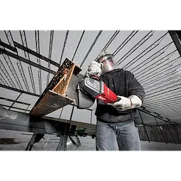 A worker uses the M18 FUEL 7” / 9” Large Angle Grinder (LAG) to cut metal, producing sparks inside a steel frame structure.