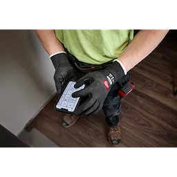 Cut Level 1 Nitrile Dipped Gloves w/ WEAR-DEFENSE Protection worn while using a smartphone over wood flooring.
