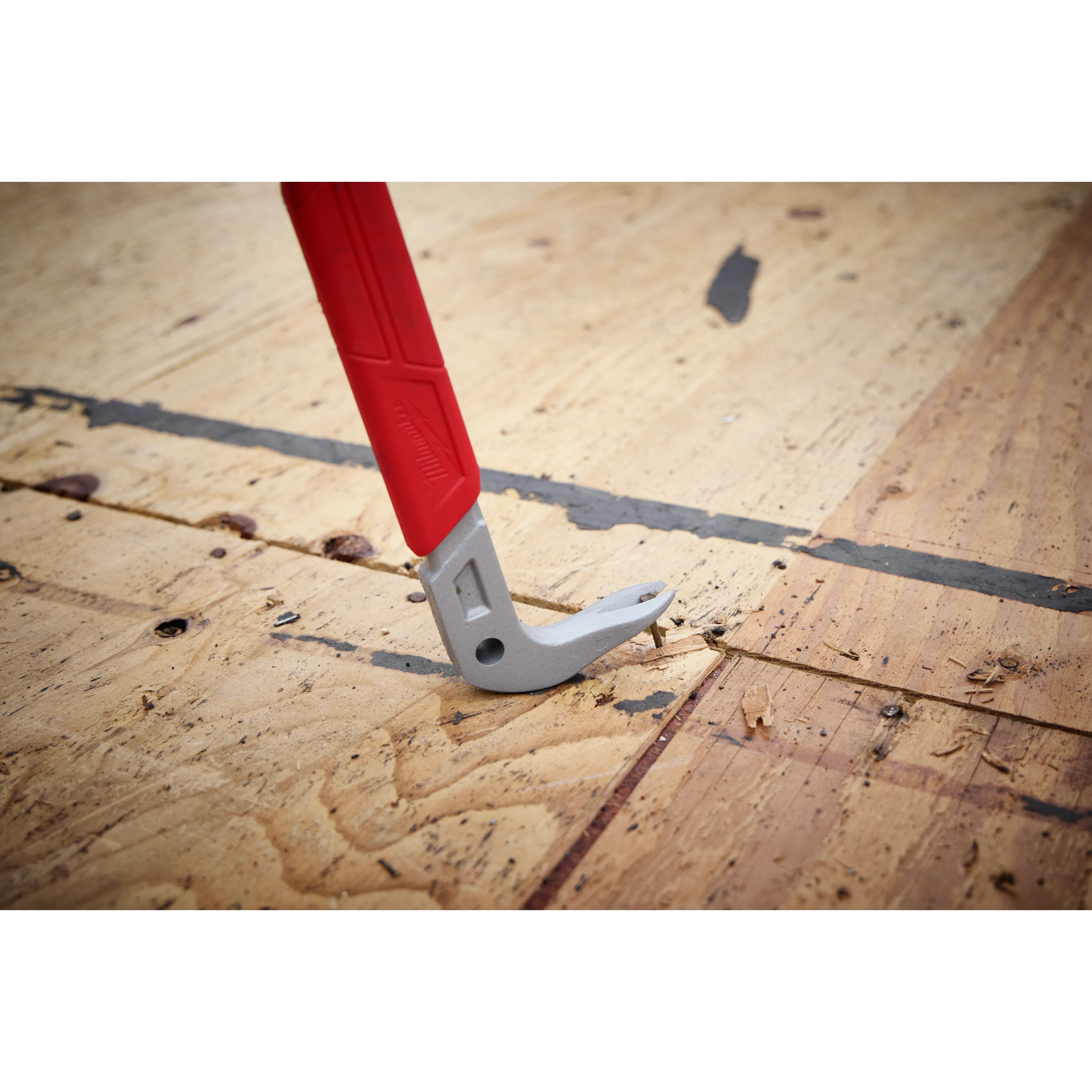 The 16" Molding Puller has a metal prying end with a red handle designed for removing moldings and trim from wooden surfaces. The tool is shown in use on a wooden floor.