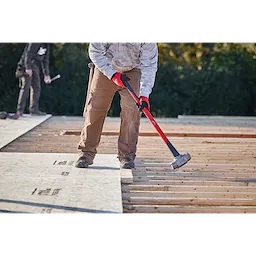 A worker using an 8lb sledgehammer (34" handle) to secure plywood sheets on a construction site.