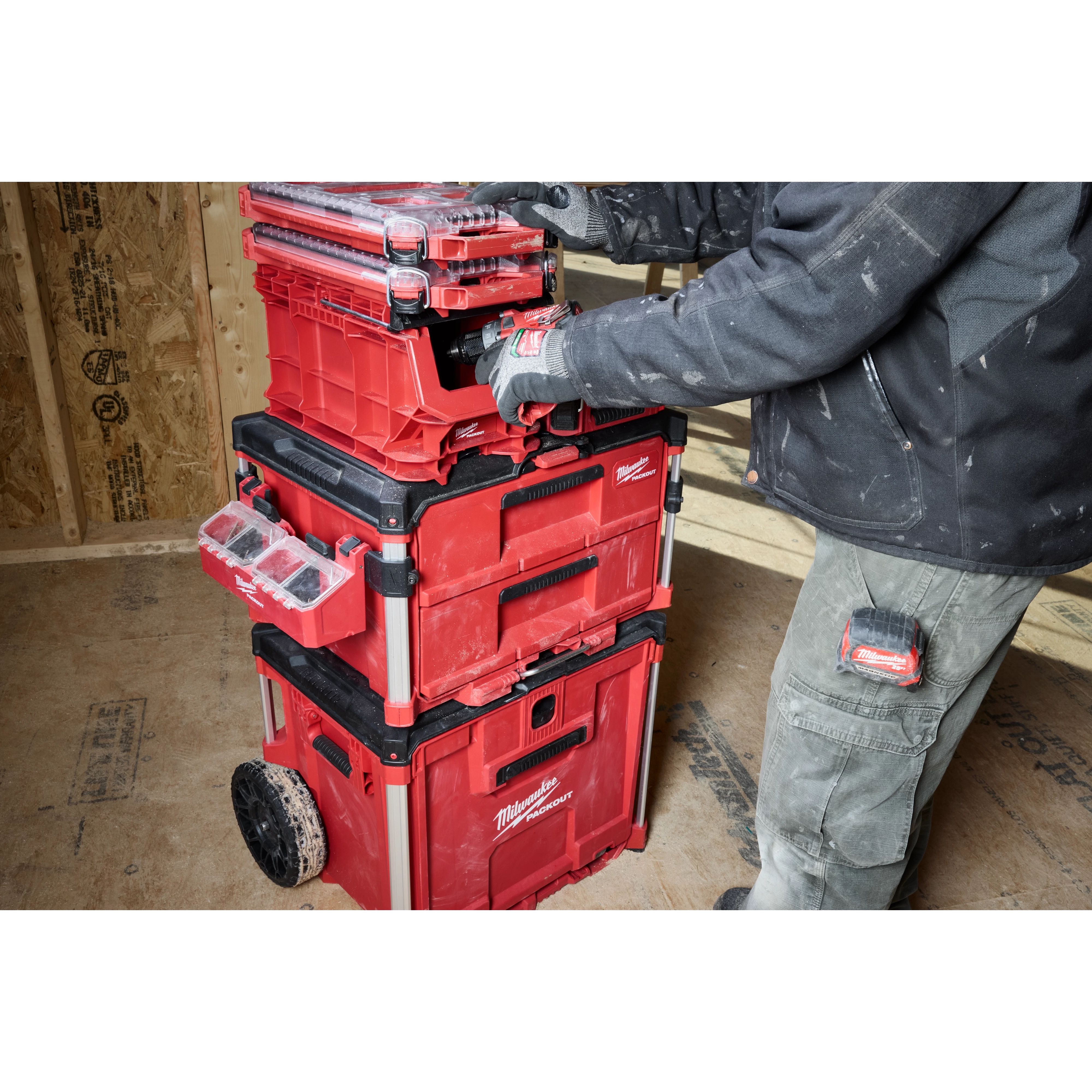 A person organizing tools in a red PACKOUT Compact Crate system with multiple stacked storage compartments and wheeled base.