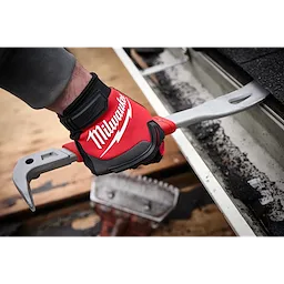 A person wearing red Milwaukee gloves uses the 16" Molding Puller tool to remove roofing materials. The puller has a silver metallic finish with a hooked end designed for prying. Roofing debris is visible in the background.