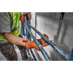 Worker wearing Goatskin Leather Gloves handling blue metal scaffolding. Worker wears a yellow safety vest and grey shirt.