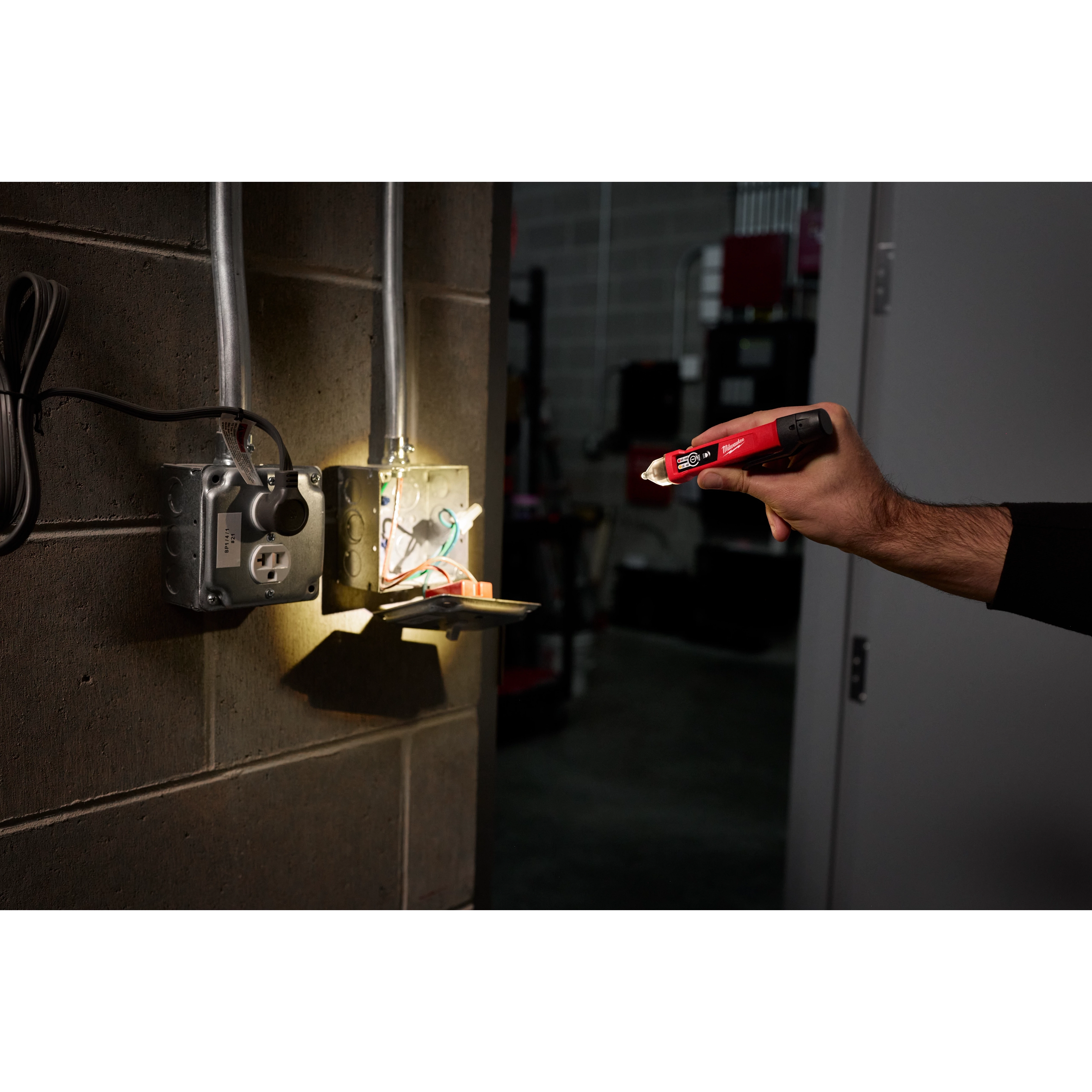 A person holds a Dual Range Voltage Detector with LED near an open electrical box. The device is illuminating the inside of the box.