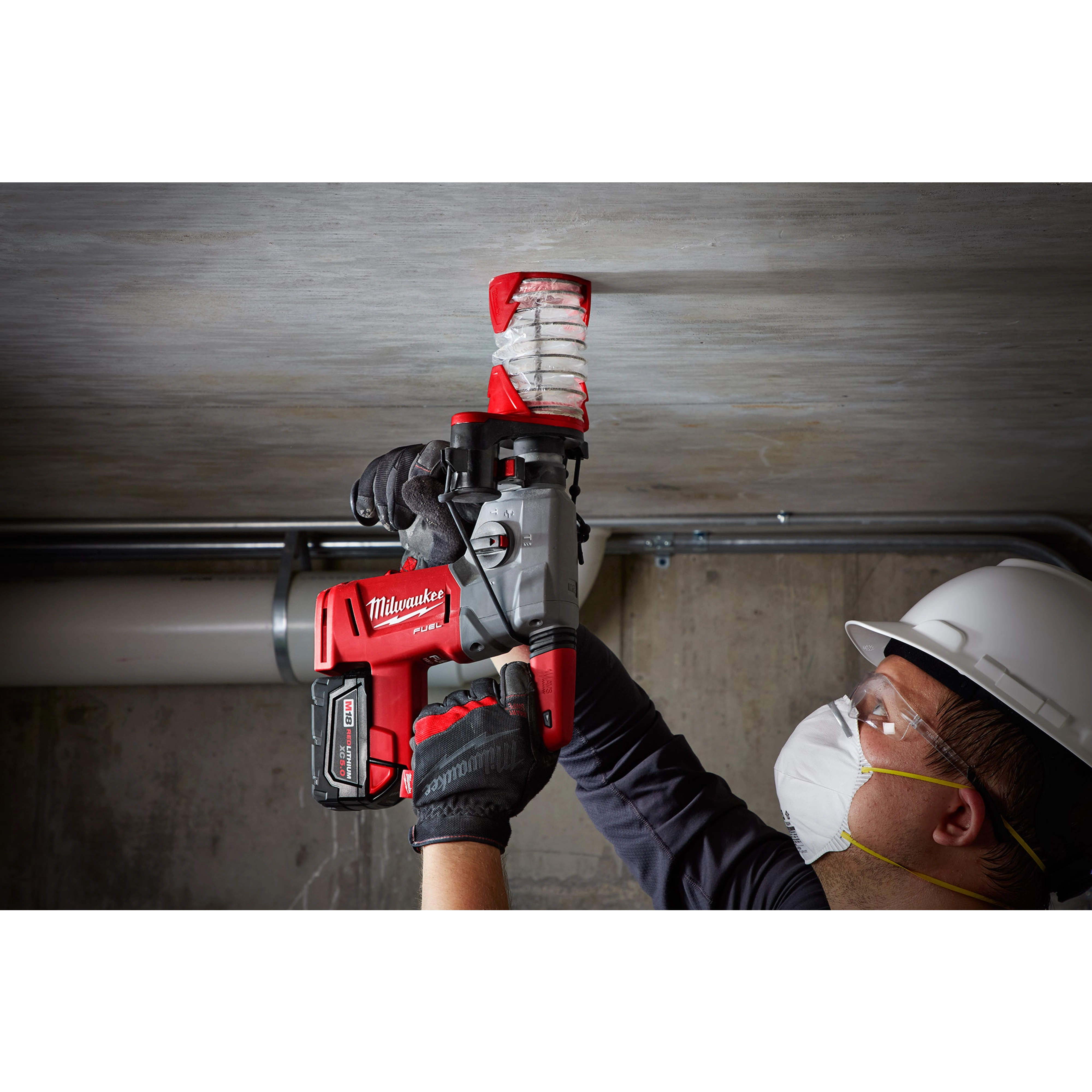 A worker is using the SDS%2B DUST TRAP Drilling Shroud Bulk 10 to drill into a concrete ceiling, attached to a red and black power drill.