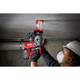 A worker is using the SDS%2B DUST TRAP Drilling Shroud Bulk 10 to drill into a concrete ceiling, attached to a red and black power drill.