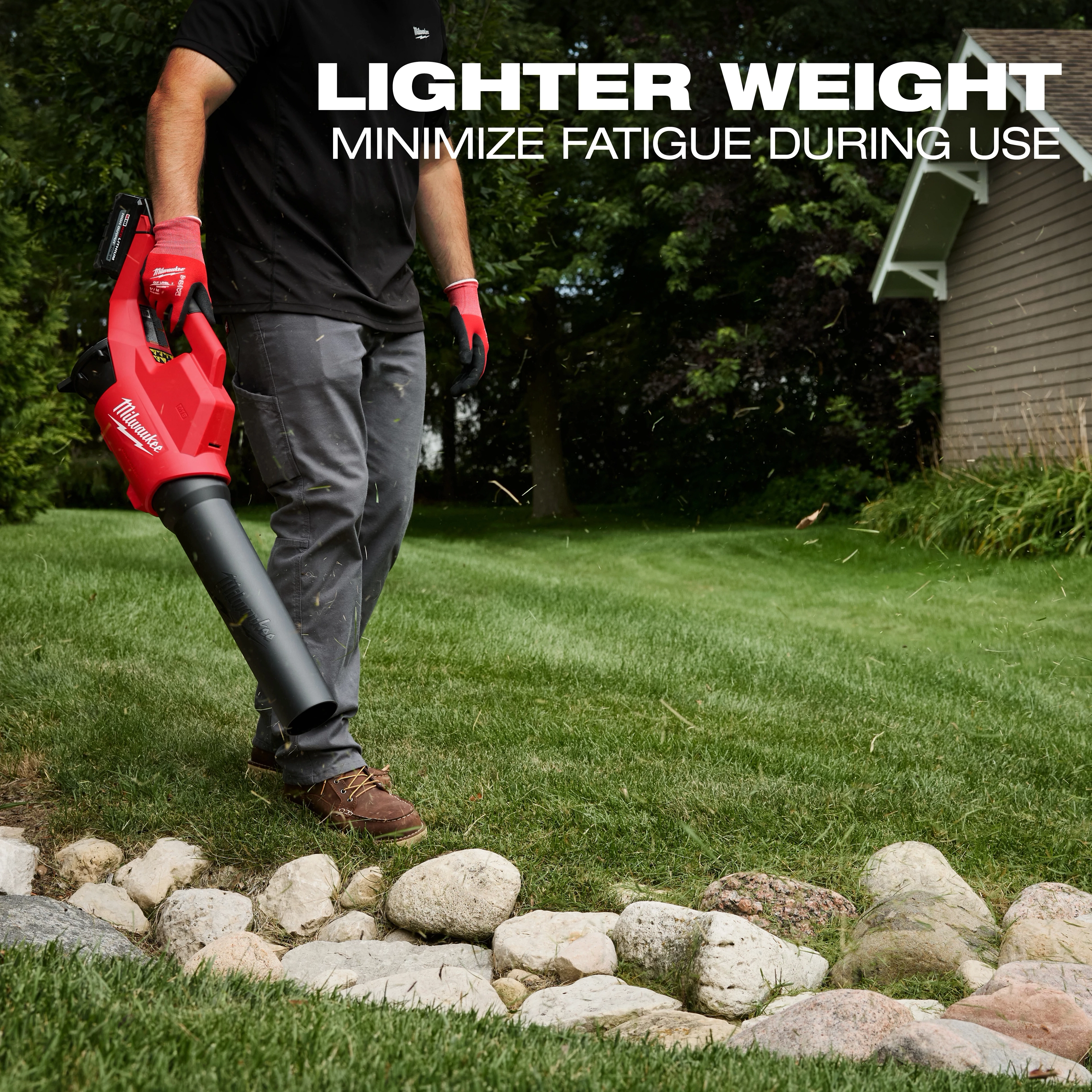 A person uses the Milwaukee M18 Brushless Blower to clear debris from a grassy area bordered by rocks. The text above the person reads, "Lighter weight, minimize fatigue during use."