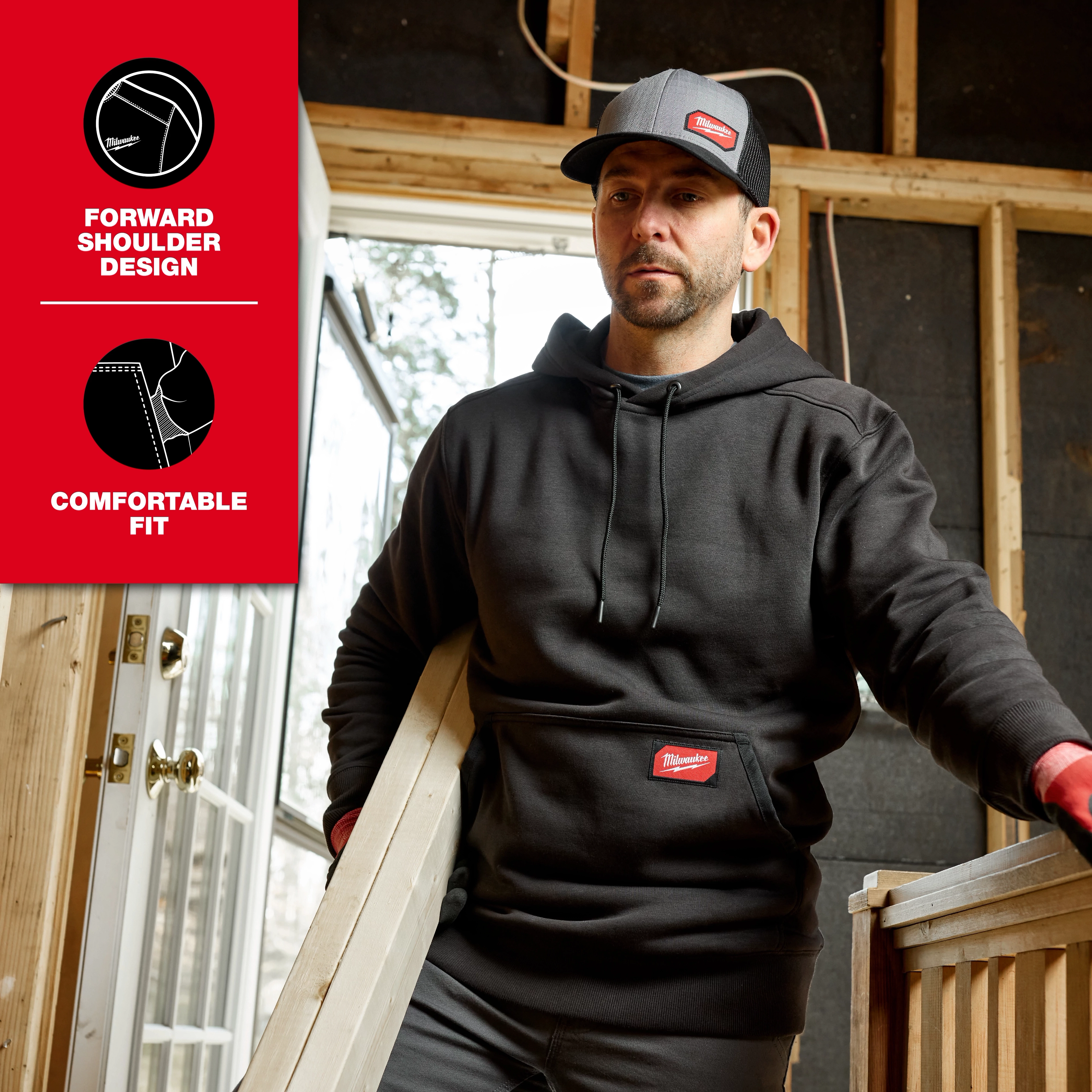Person wearing a black FREEFLEX Pullover Hoodie while carrying a board inside a partially built room.