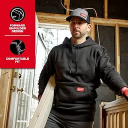 Person wearing a black FREEFLEX Pullover Hoodie while carrying a board inside a partially built room.