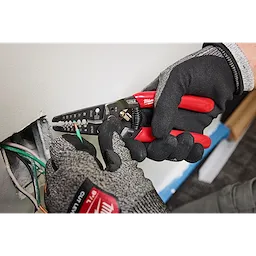 8-20 AWG Dipped Grip Wire Stripper & Cutter being used by a gloved hand to strip a wire near a wall opening.