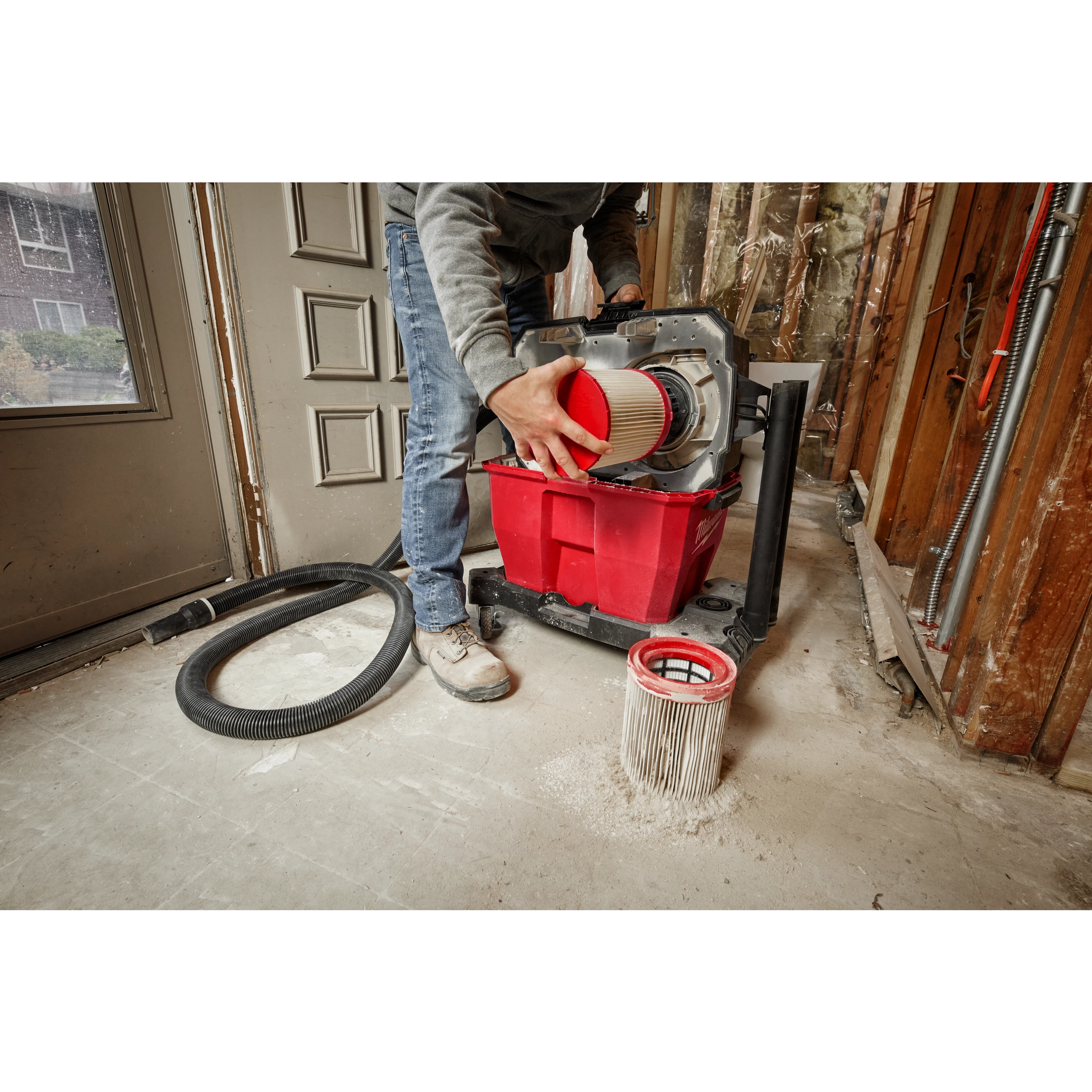 A person changes the HEPA filter of a wet/dry vacuum in a construction setting, with another filter on the floor.