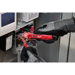 A person wearing black and gray gloves uses a red Voltage Detector w/ LED to check electrical wires inside an open electrical box.