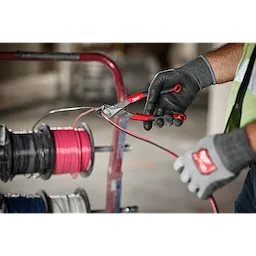 A person in work gloves uses the 8" Diagonal Comfort Grip Pliers (USA) to cut a pink wire, with wire spools in the background.