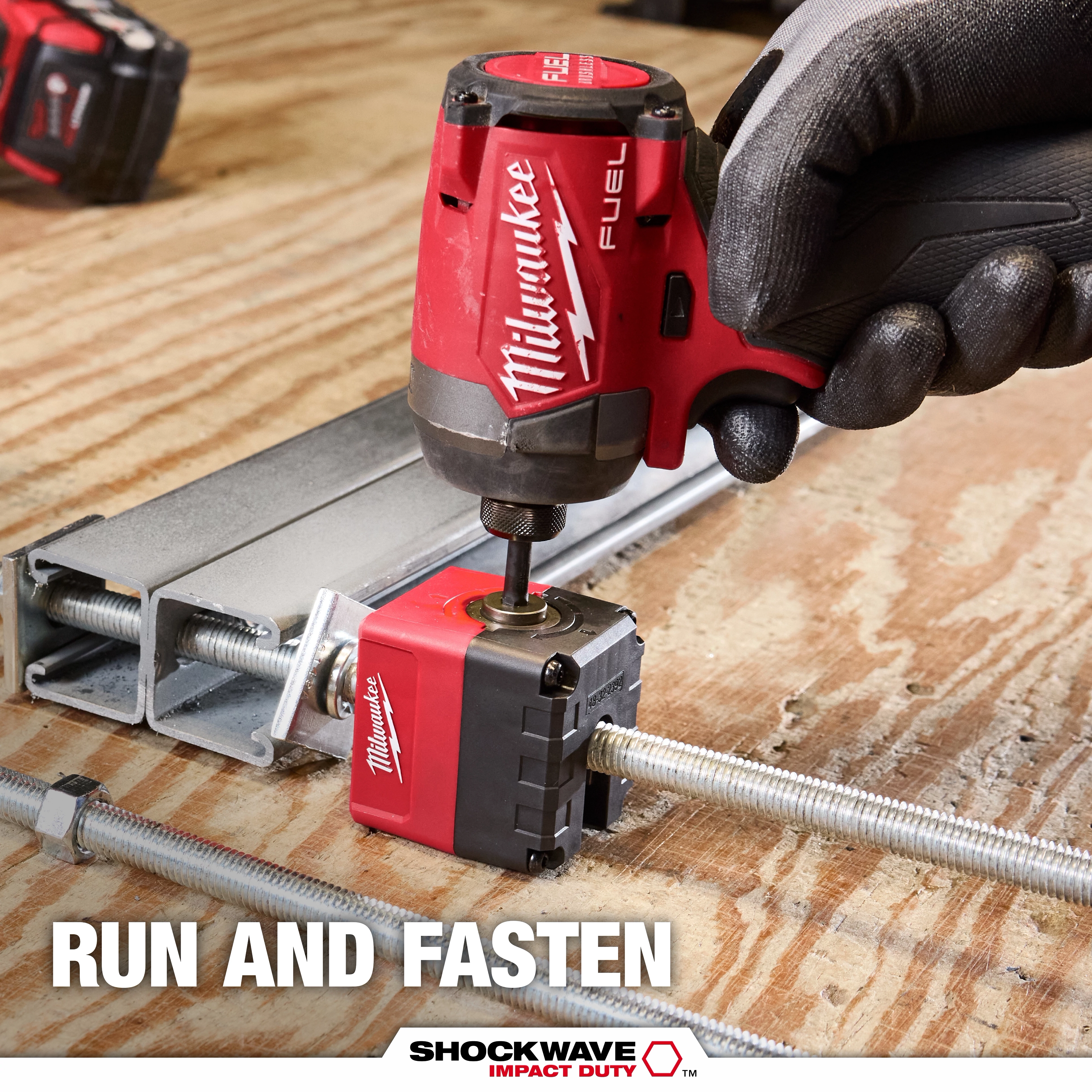 Gloved hand using SHOCKWAVE Impact Duty 1/2" Threaded Rod Nut Runner on a threaded rod over a wooden surface.