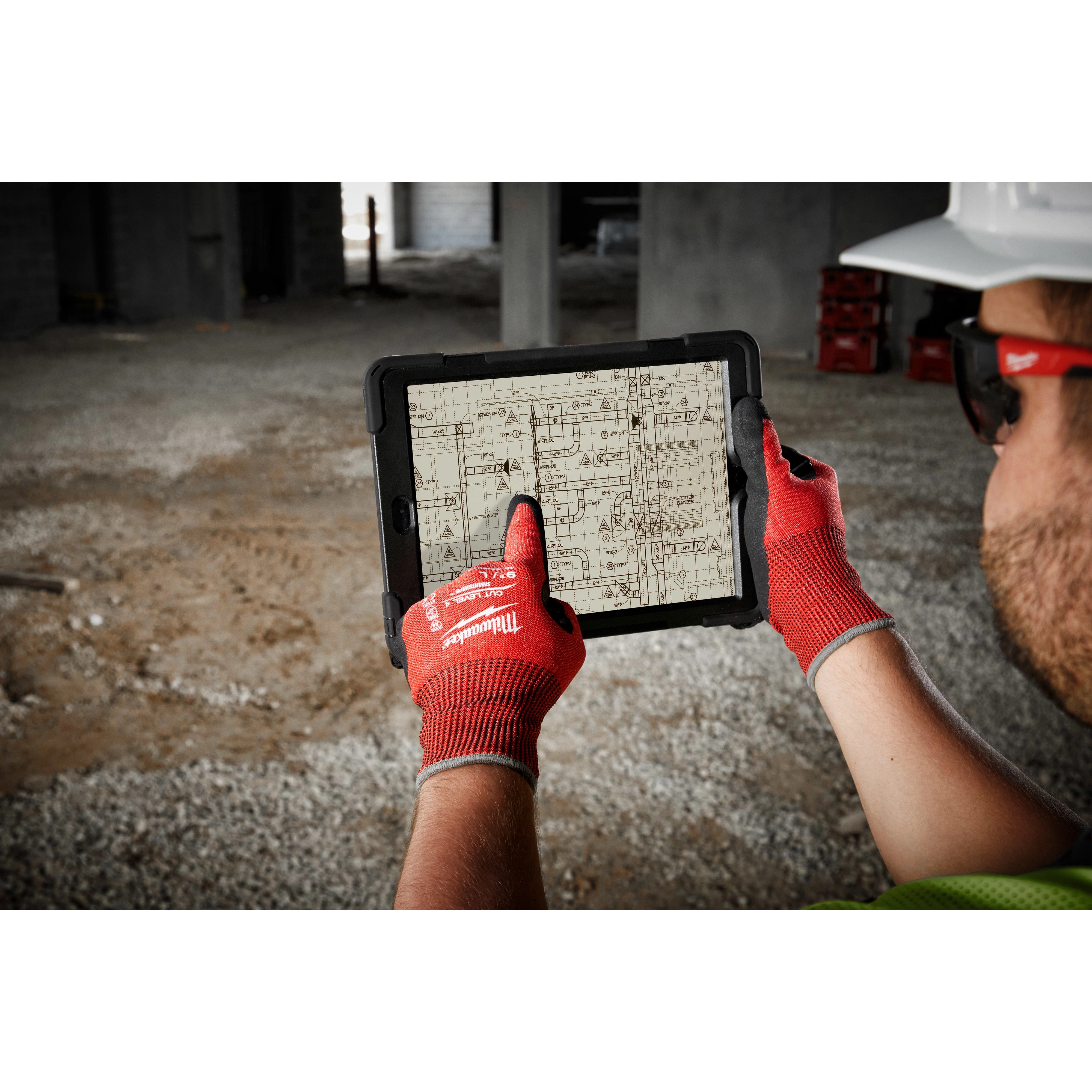 A person wearing Cut Level 4 Nitrile Dipped Glove - L uses a tablet to view construction blueprints at a worksite.