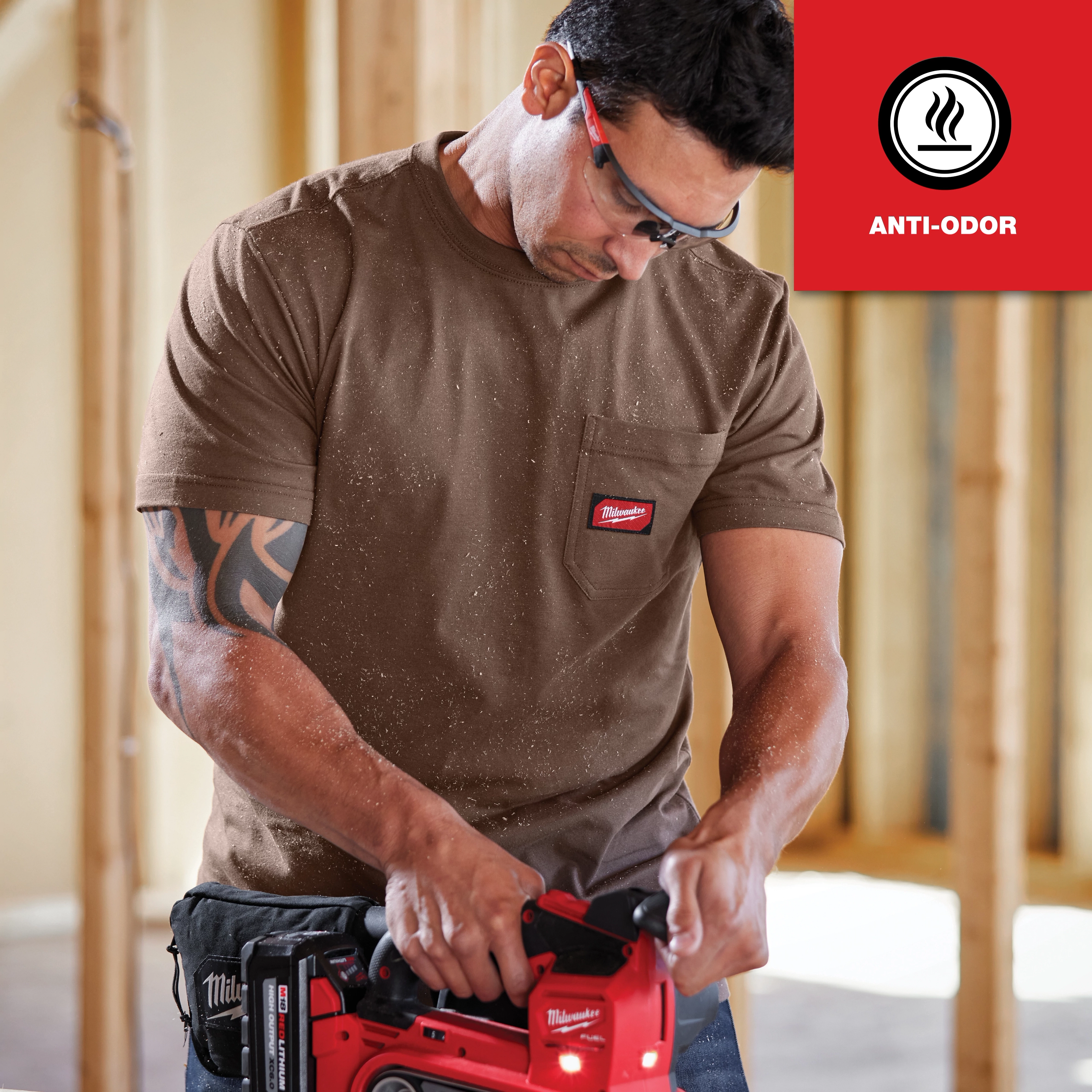 Man wearing a brown GRIDIRON Pocket T-Shirt - Short Sleeve Anti-odor while using a red power tool in a construction setting.