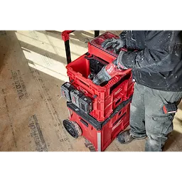 Worker using a power tool with Divider for PACKOUT XL Crate integrated in a red modular toolbox system with crates on a job site.