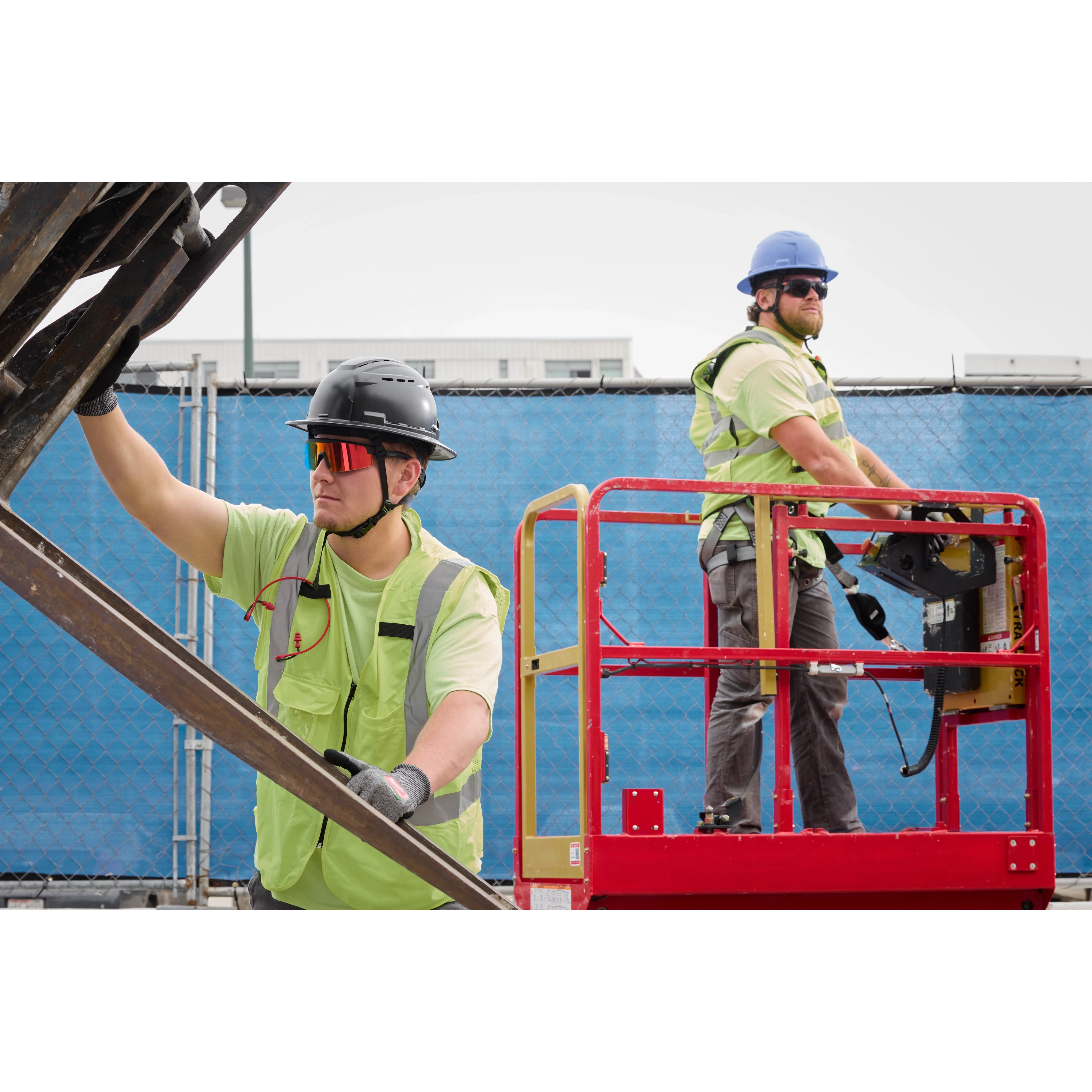 Construction workers wearing Wrap-Around Safety Glasses with red Mirrored Anti-Scratch Lenses operate a scissor lift. They are on a building site and wear protective gear, including helmets and high-visibility vests, emphasizing safety protocols.