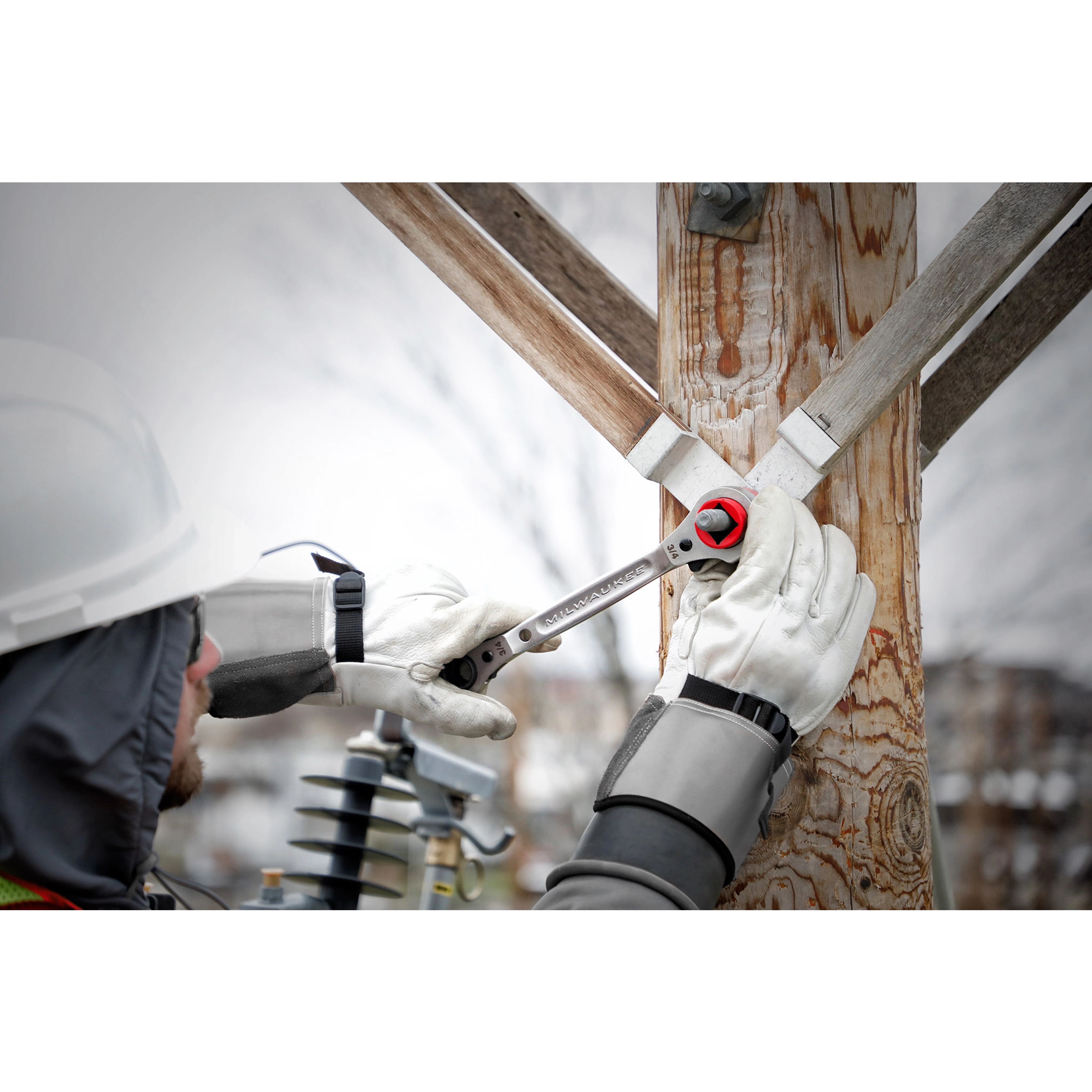 Lineman uses the Lineman's 5-in-1 Ratcheting Wrench to tighten a bolt on a wooden utility pole, wearing safety gloves and helmet.
