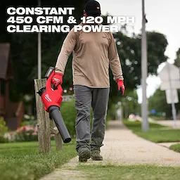 A person uses the Milwaukee M18 Brushless Blower to clear a sidewalk. The blower delivers 450 CFM and 120 MPH clearing power.