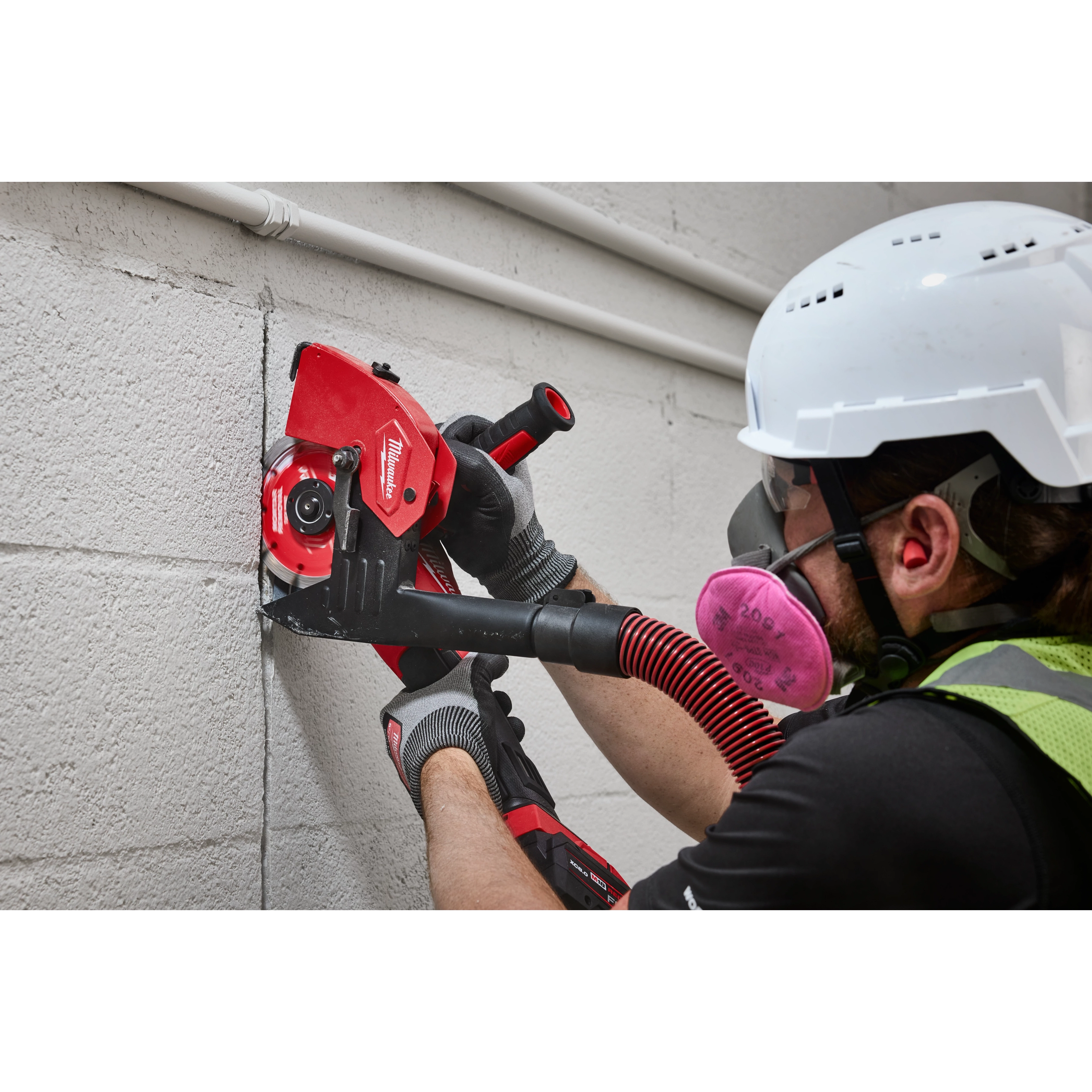 A construction worker uses a power tool equipped with a Milwaukee 6" Tuckpointing Dust Shroud to cut through a concrete wall. The dust shroud helps manage debris during the cutting process.