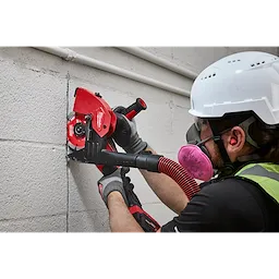 A construction worker uses a power tool equipped with a Milwaukee 6" Tuckpointing Dust Shroud to cut through a concrete wall. The dust shroud helps manage debris during the cutting process.