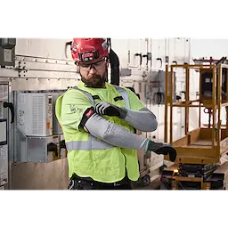 Worker wearing high-visibility vest adjusts Cut Level 6 Protective Sleeves in an industrial setting with control panels and scaffold.