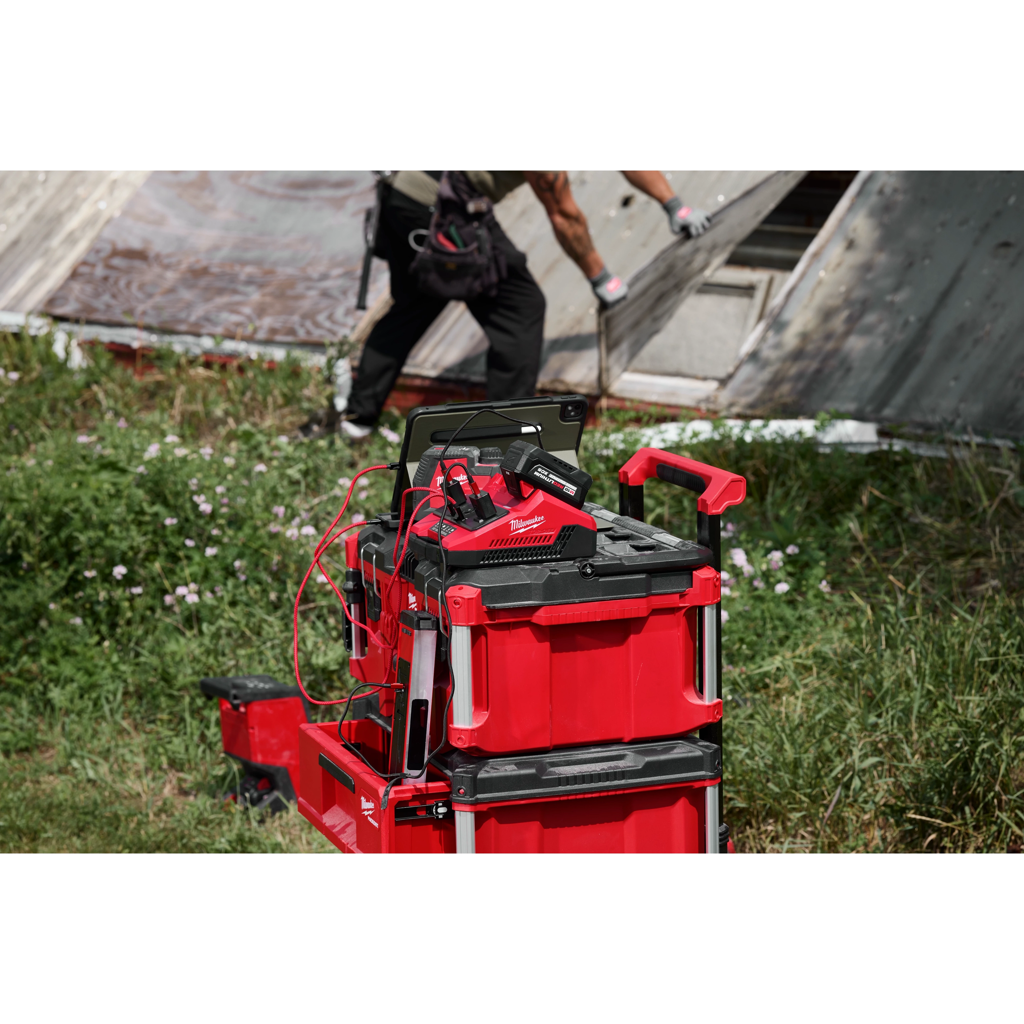 M18 TOP-OFF 350W Power Supply & Charger w/ PACKOUT Compatibility stacked on red tool boxes outdoors.