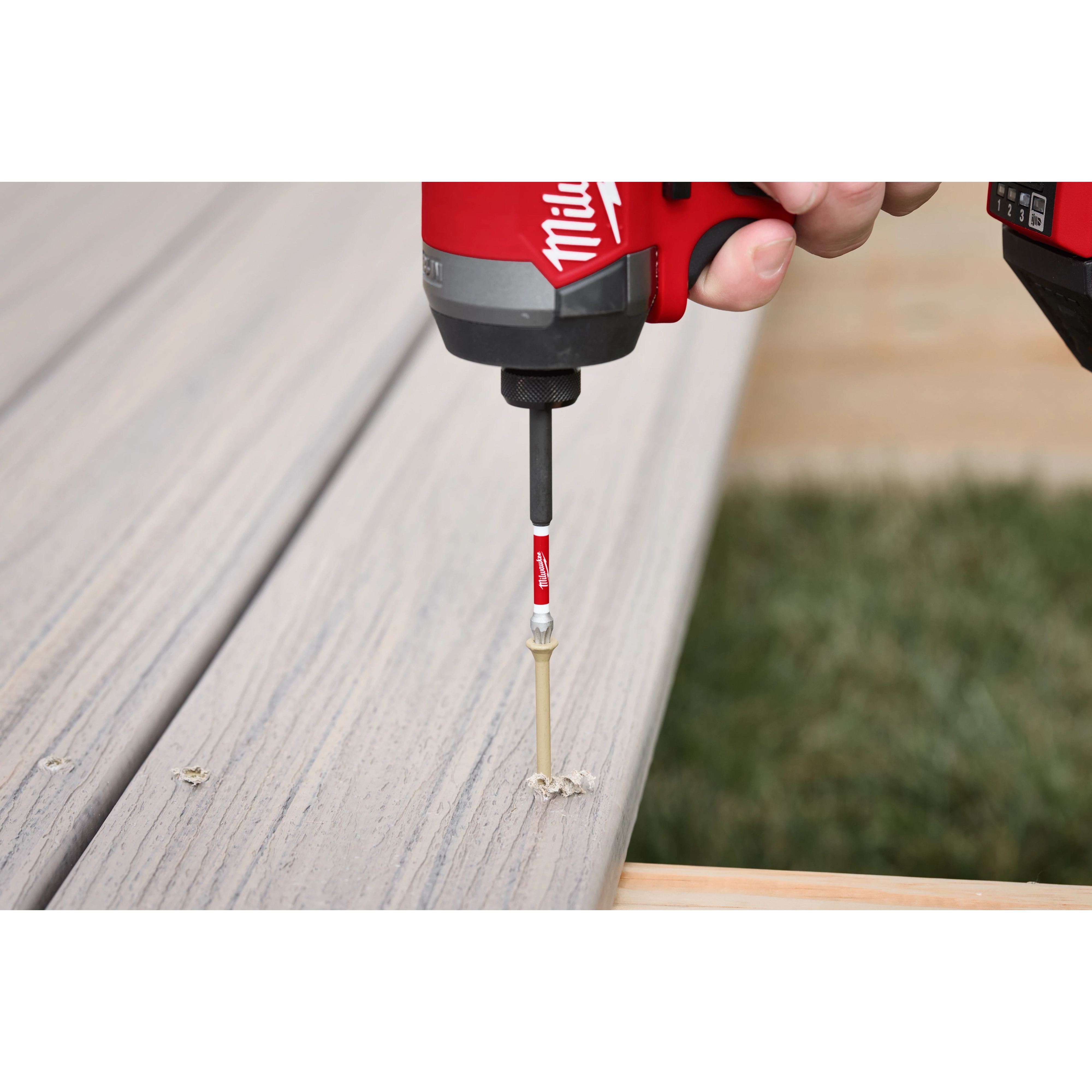 A hand using a red and black power drill with a SHOCKWAVE™ 3-1/2" Impact Torx® T25 Power Bit to drive a screw into a wooden plank. The image shows the bit in action, securing the screw into the wood.