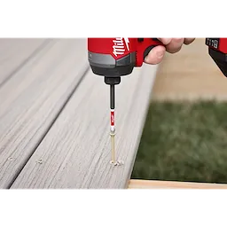 A hand using a red and black power drill with a SHOCKWAVE™ 3-1/2" Impact Torx® T25 Power Bit to drive a screw into a wooden plank. The image shows the bit in action, securing the screw into the wood.