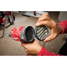 A person in a red shirt holds the M18™ Brushless Precision Blower with one hand while removing its filter cover with the other. The tool is red and black with a visible interior filter.