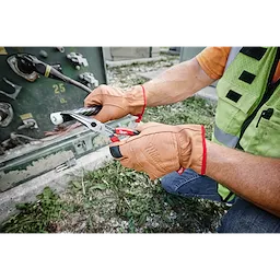 Person wearing Goatskin Leather Gloves - XL while using pliers to work with electrical cables outdoors.