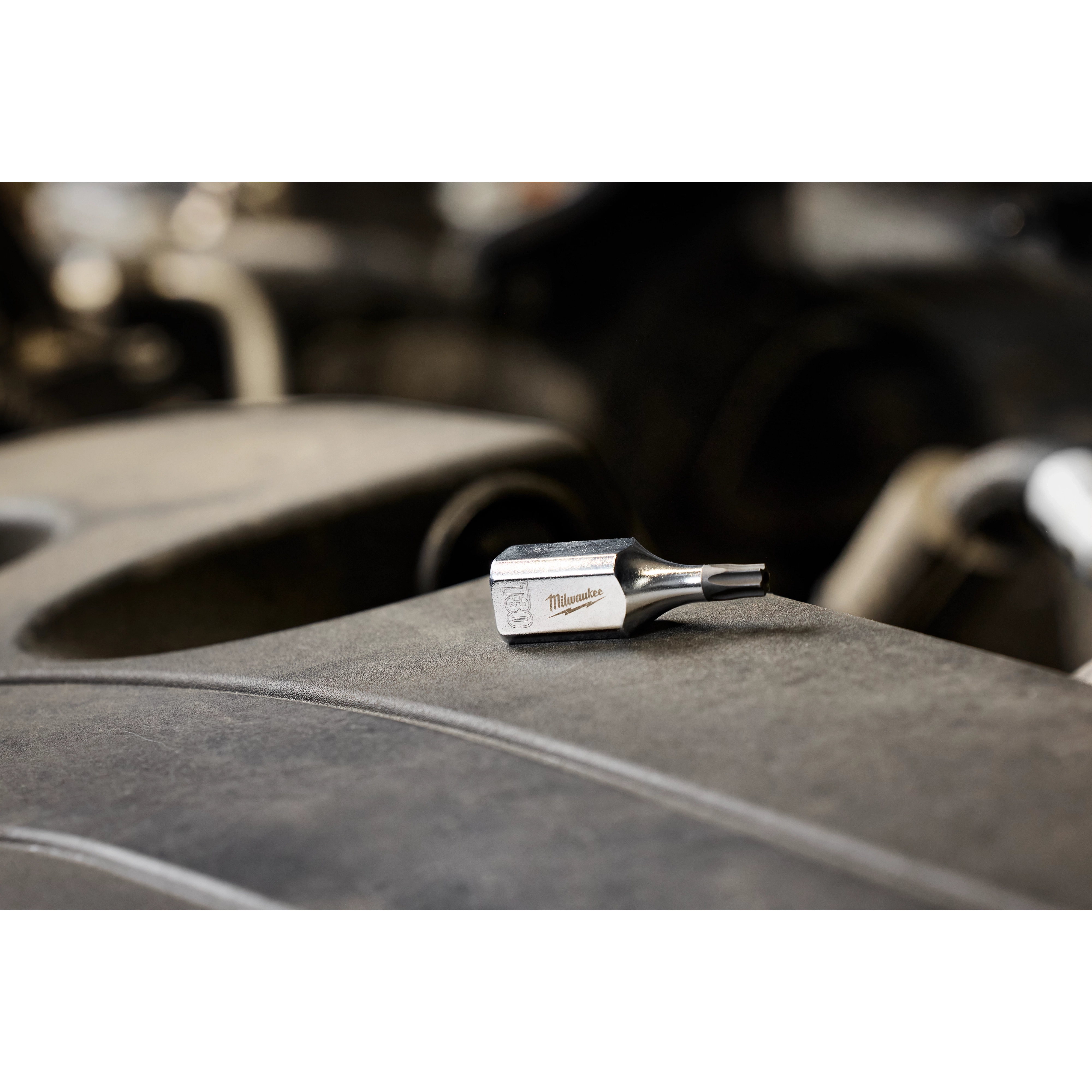 The 3/8" Drive T30 Tamper-Proof TORX Bit Socket is displayed on a gray surface with a blurred background. The small, metal bit socket features a TORX head and is designed for secure, tamper-proof fastener removal.