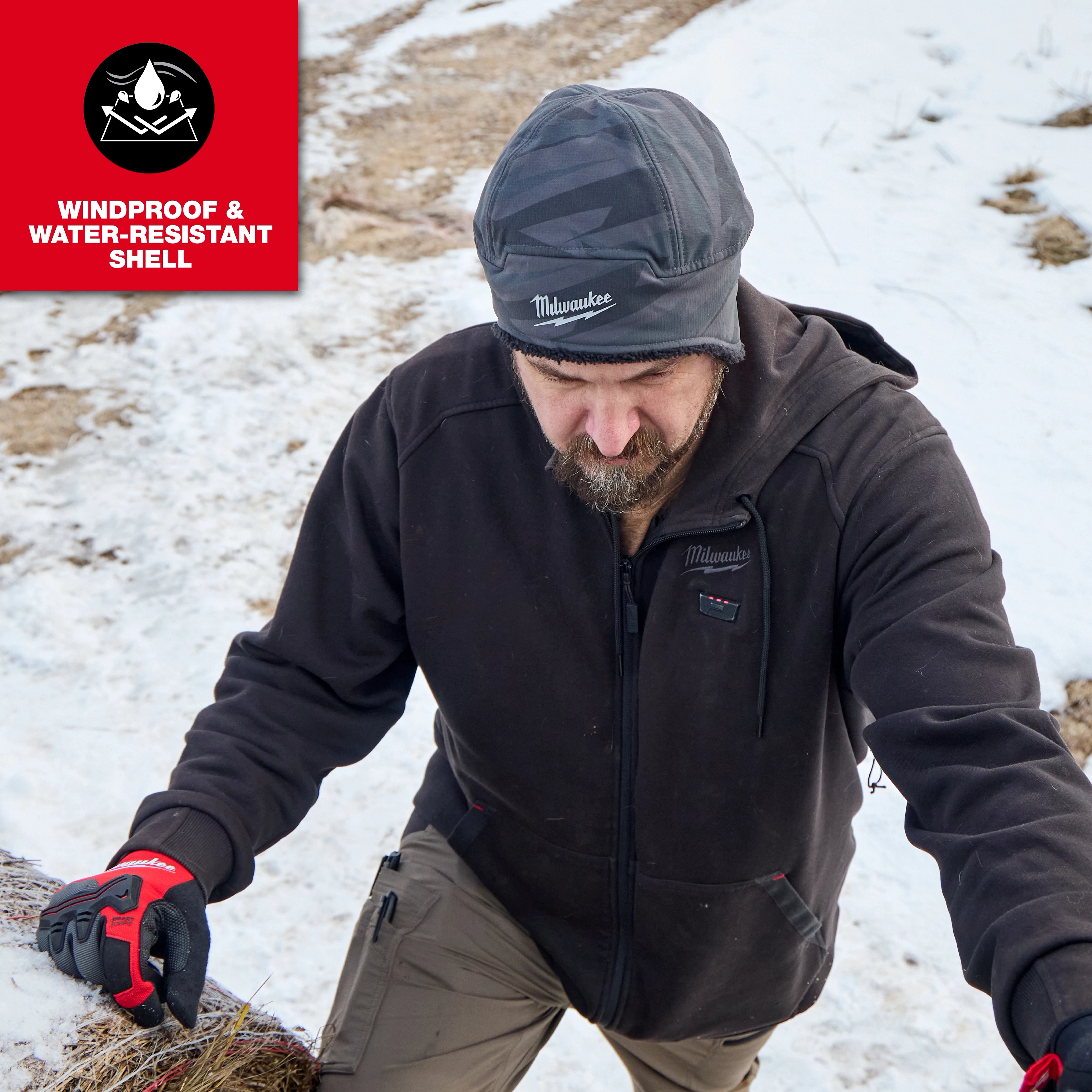 Person outdoors in snow wearing a Milwaukee Sherpa-Lined Beanie and work jacket, climbing a snowy slope.