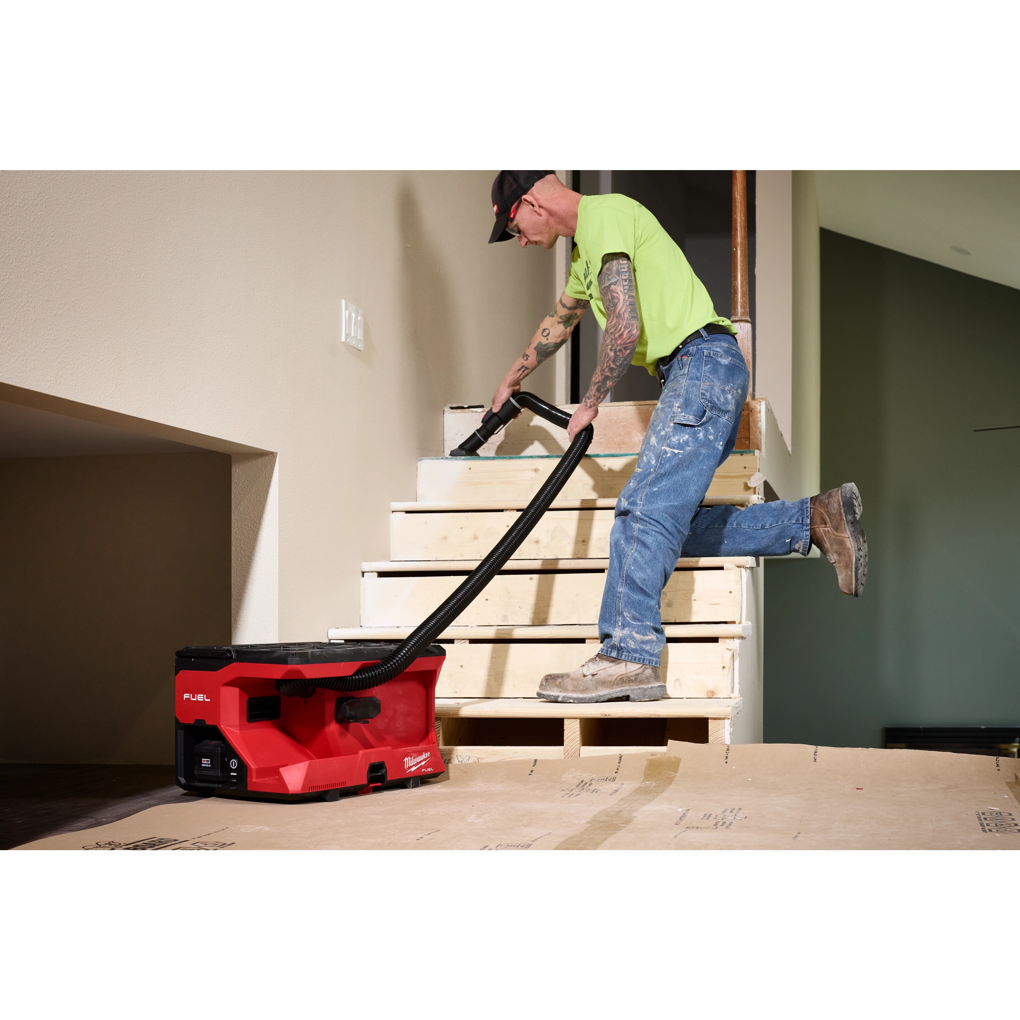 Worker using an M18 FUEL 4 Gallon Wet/Dry Vacuum w/ PACKOUT Compatibility & VACLINK on unfinished wooden stairs.