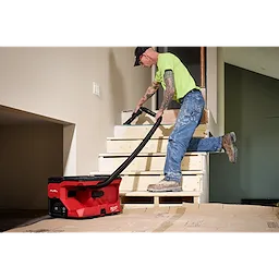Worker using an M18 FUEL 4 Gallon Wet/Dry Vacuum w/ PACKOUT Compatibility & VACLINK on unfinished wooden stairs.
