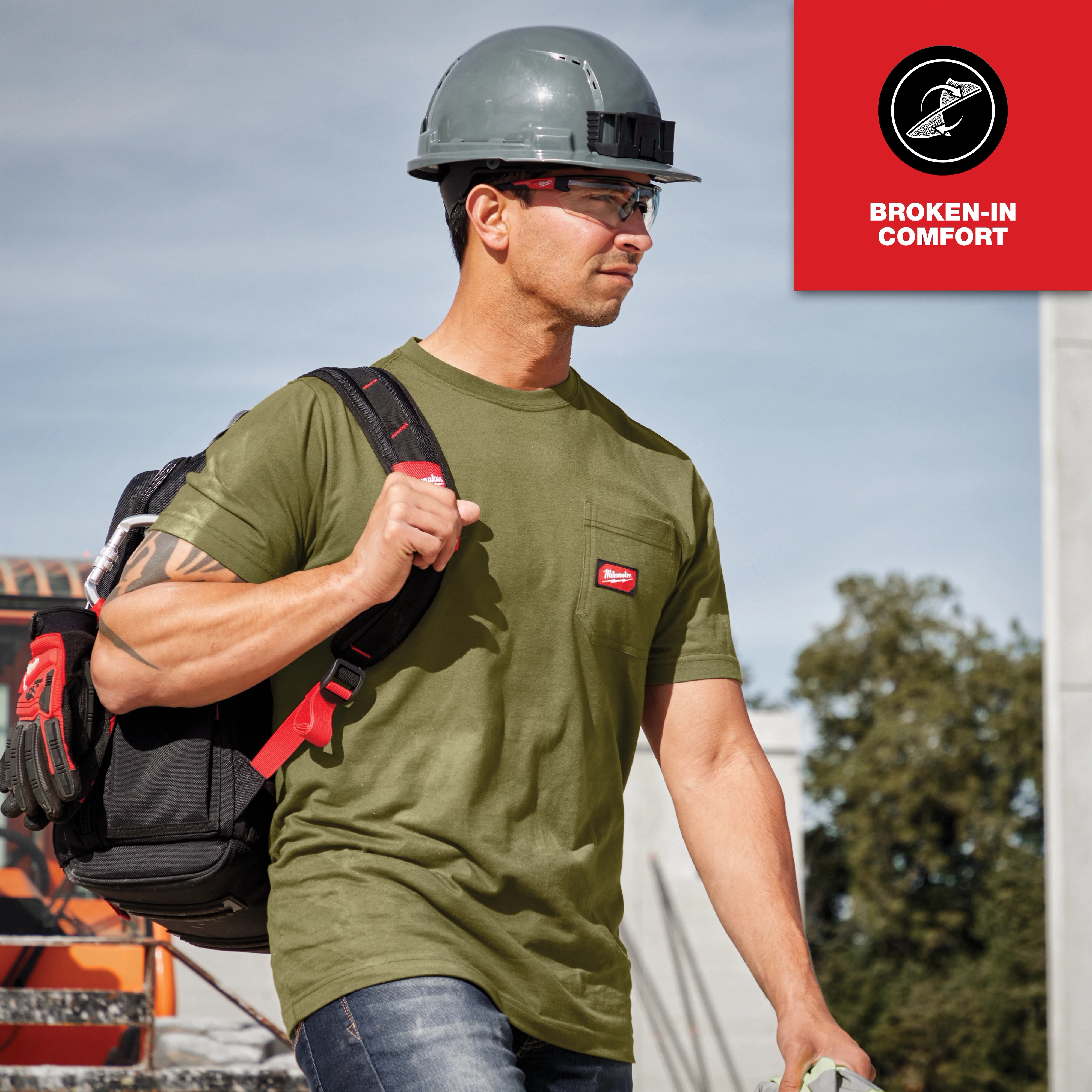 Man wearing hard hat and carrying tools in a green GRIDIRON Pocket T-Shirt - Short Sleeve with a red patch on the chest.