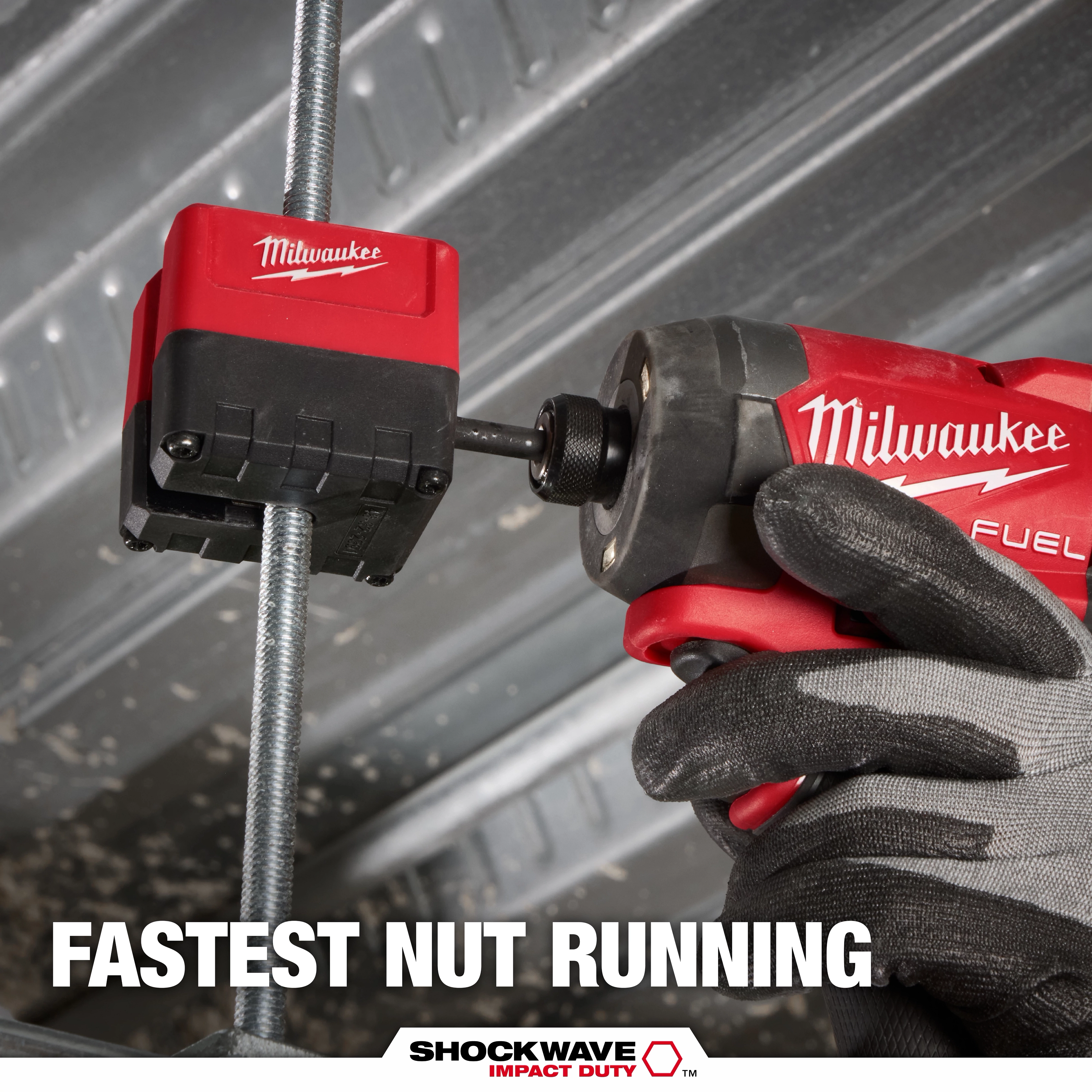 The Milwaukee SHOCKWAVE™ Impact Duty 3/8" Threaded Rod Nut Runner attaches to a threaded rod. A hand wearing a black glove grips a Milwaukee Fuel power drill connected to the nut runner. Text below reads "FASTEST NUT RUNNING" and "SHOCKWAVE™ Impact Duty" in white and red font.